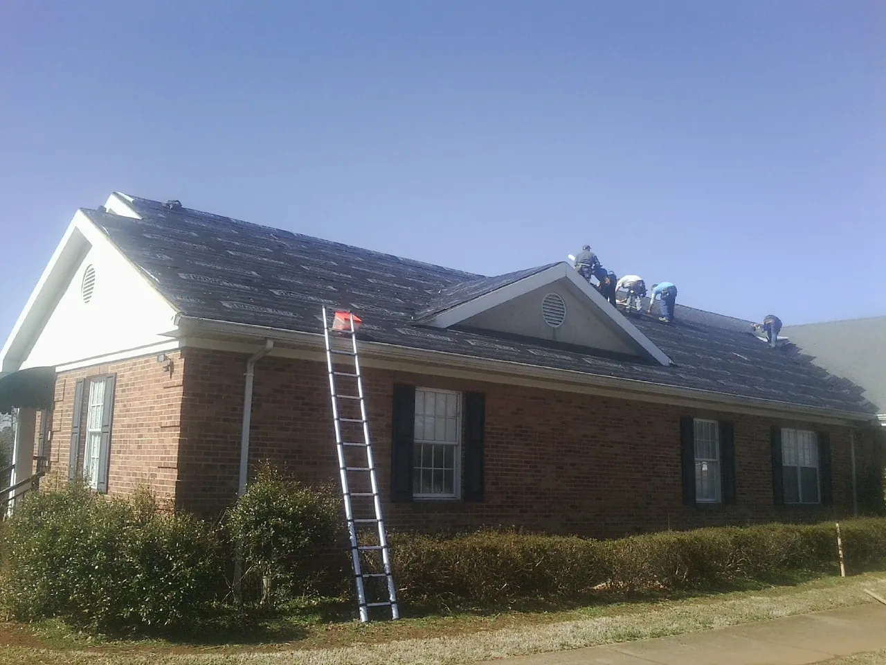 Crew tearing shingles off a brick ranch roof with a ladder set — Emergency Roof Repair work by our crew in Basin