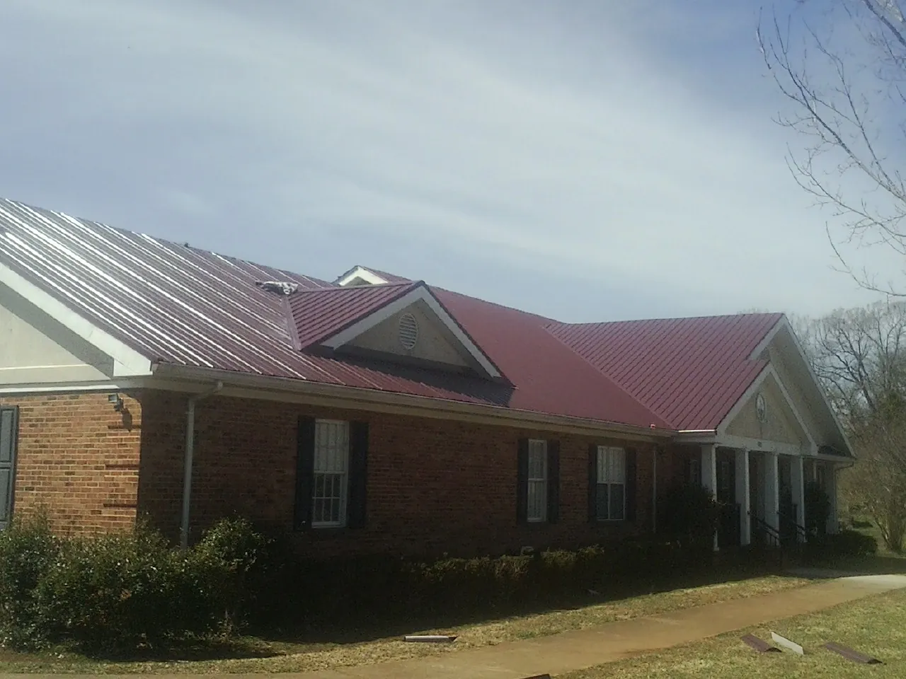 Red metal roof with gabled entries on a long brick building, from a Hail Damage Roof Repair job in Basin