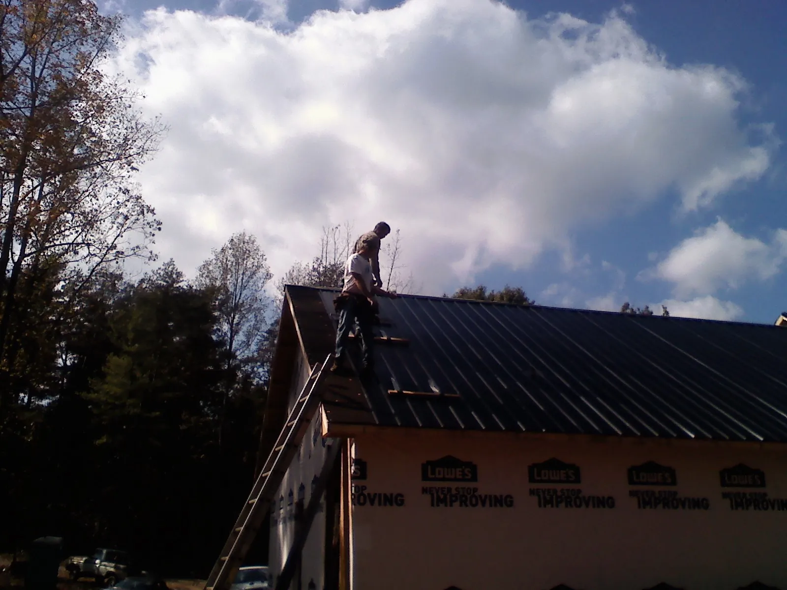 Roofer fastening dark metal panels high against a cloudy sky, from a Roof Inspection job in Basin